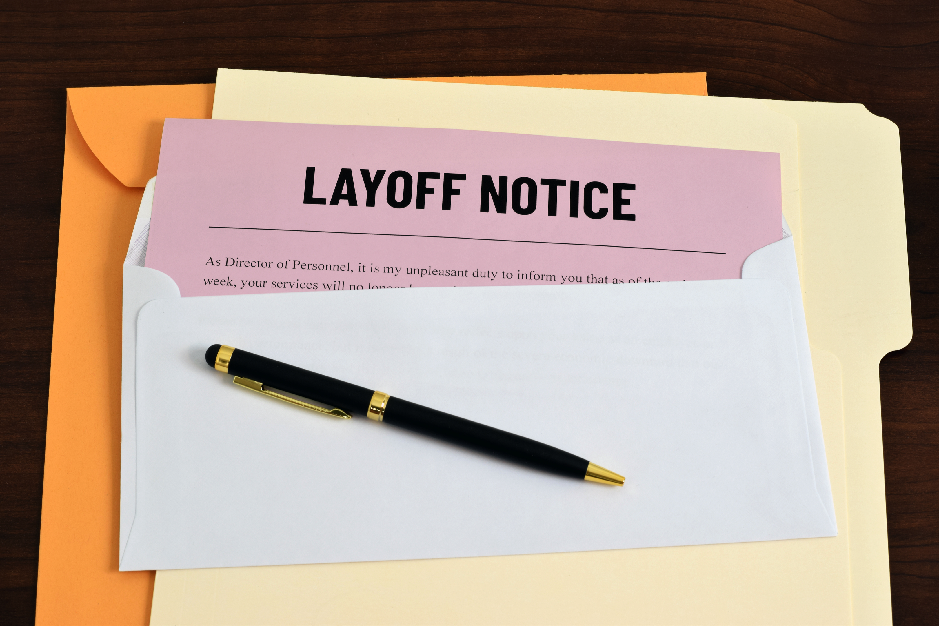 Layoff notice in envelope with pen and folders, symbolizing employee termination and legal rights support from Hershey Law