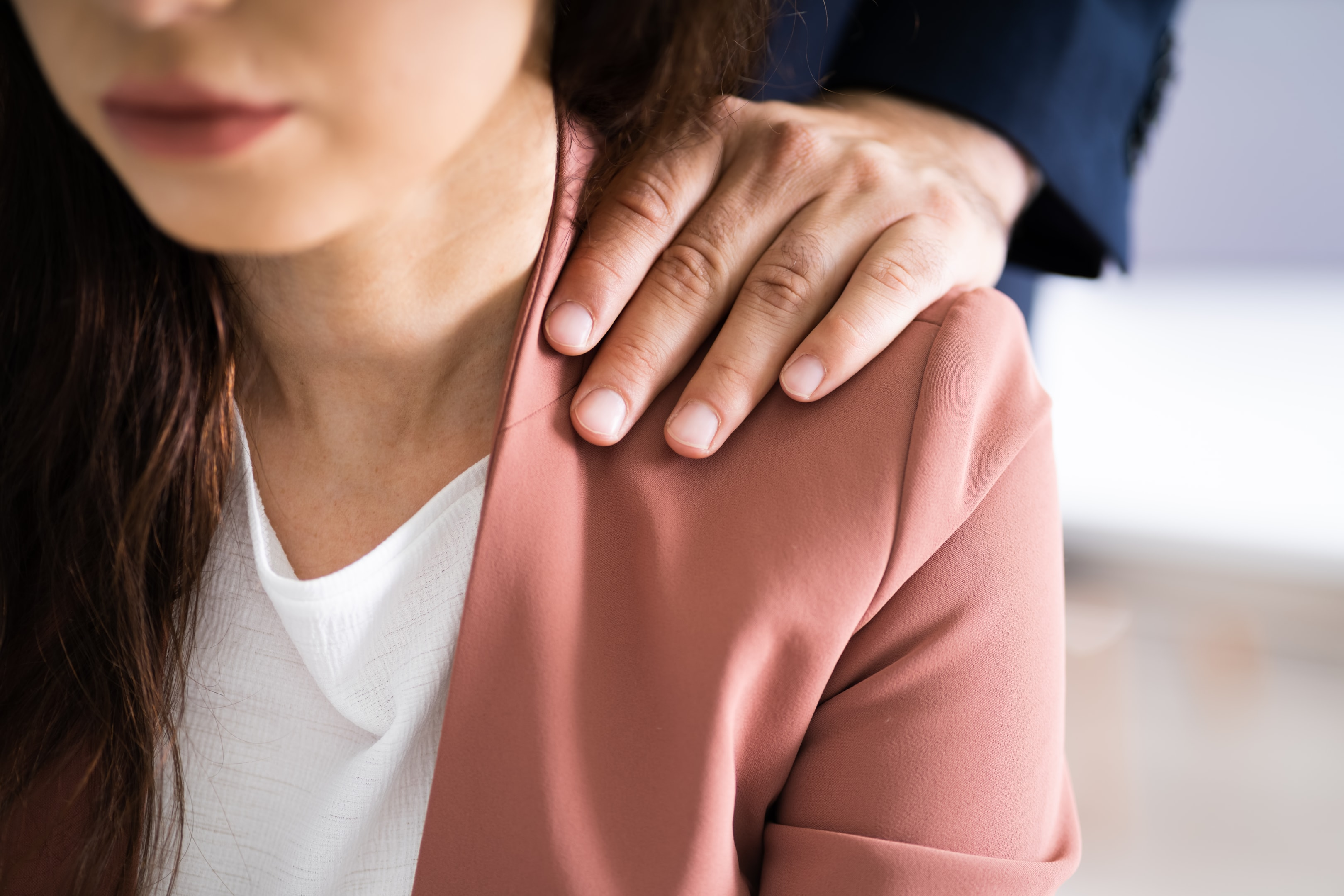 Close-up of an unwanted hand on a woman's shoulder, symbolizing warning signs of sexual harassment in the workplace.
